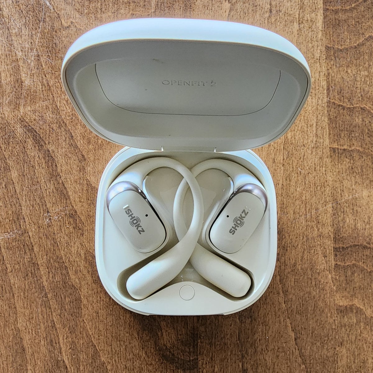 SHOKZ OpenFit 2 open-ear earbuds in an open charging case on a wooden table.